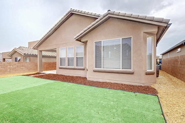 rear view of house featuring a fenced backyard, a tiled roof, and stucco siding