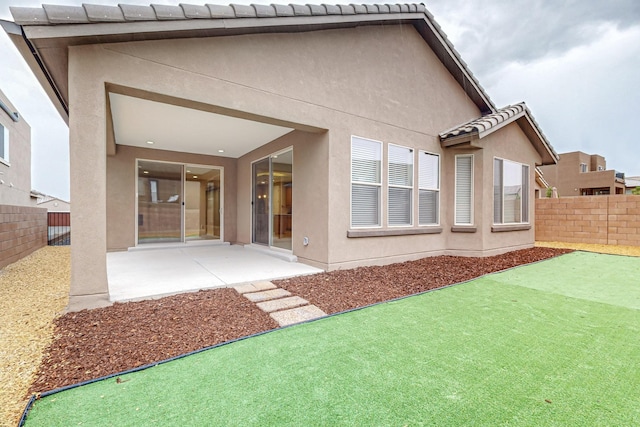 rear view of property with a tiled roof, a patio area, a fenced backyard, and stucco siding