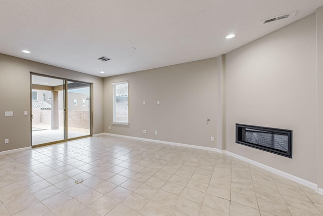 spare room featuring a glass covered fireplace, visible vents, and baseboards