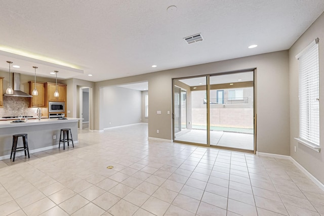 unfurnished living room with a healthy amount of sunlight, visible vents, baseboards, and light tile patterned floors