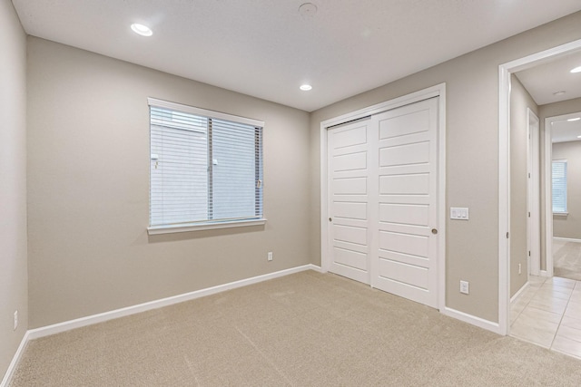 unfurnished bedroom with a closet, light carpet, and baseboards