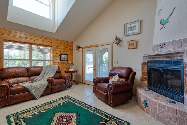 living room with french doors, high vaulted ceiling, light tile patterned floors, wood walls, and a tile fireplace