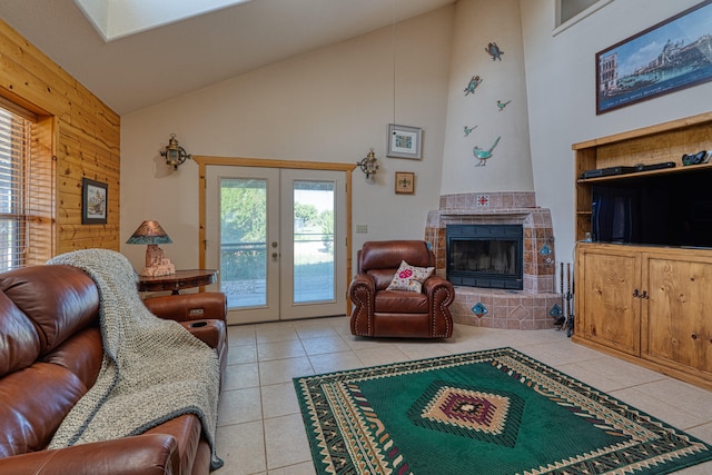 tiled living room featuring wood walls, high vaulted ceiling, a large fireplace, and french doors