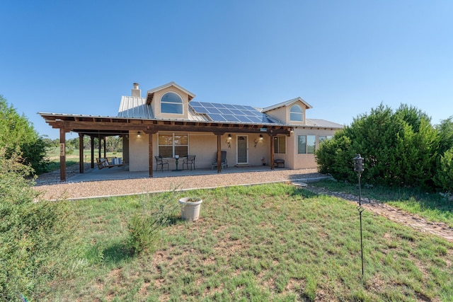 back of house featuring roof mounted solar panels, a patio area, metal roof, and a lawn