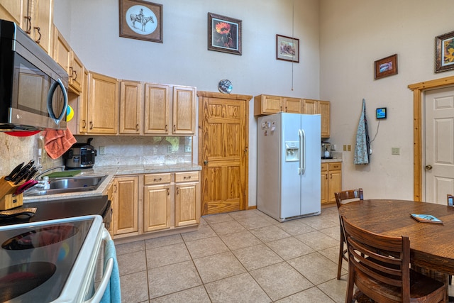 kitchen with a towering ceiling, white refrigerator with ice dispenser, light tile patterned floors, backsplash, and sink