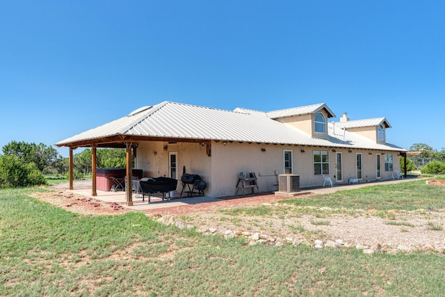 rear view of house with stucco siding, a hot tub, a patio area, central AC, and metal roof