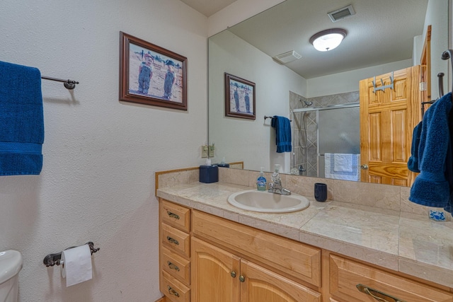 bathroom with visible vents, a tile shower, vanity, and toilet