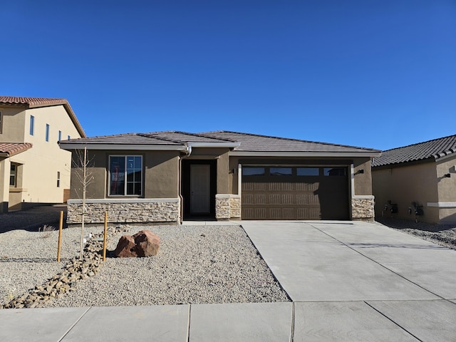 prairie-style house with a tile roof, stucco siding, concrete driveway, an attached garage, and stone siding