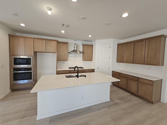 kitchen with light wood finished floors, stainless steel appliances, visible vents, a sink, and wall chimney range hood