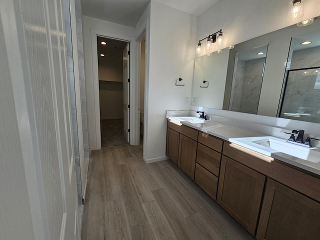 full bathroom with double vanity, wood finished floors, a sink, and a shower stall