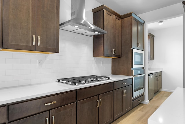 kitchen with dark brown cabinetry, stainless steel appliances, light countertops, ventilation hood, and decorative backsplash