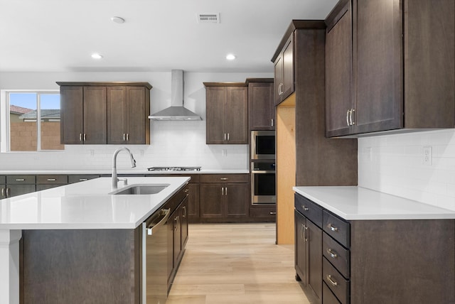 kitchen featuring visible vents, appliances with stainless steel finishes, light countertops, wall chimney range hood, and a sink