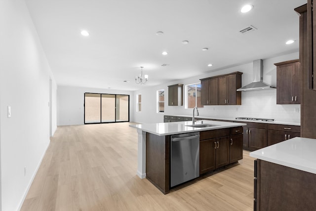 kitchen featuring an island with sink, appliances with stainless steel finishes, light countertops, wall chimney range hood, and a sink