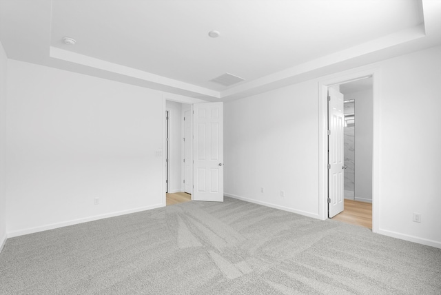 empty room with baseboards, a tray ceiling, and light colored carpet