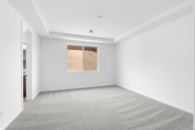 unfurnished room with a raised ceiling, visible vents, light carpet, and baseboards