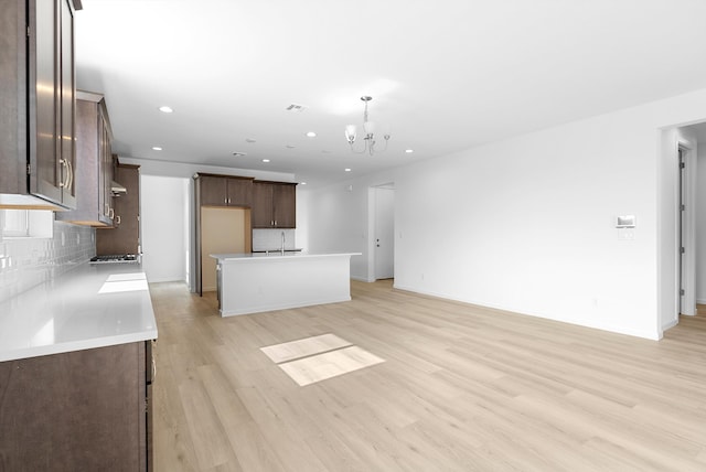 kitchen featuring light wood finished floors, tasteful backsplash, a center island with sink, open floor plan, and light countertops