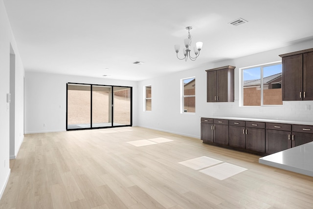 interior space with a notable chandelier, light wood finished floors, light countertops, decorative backsplash, and dark brown cabinetry