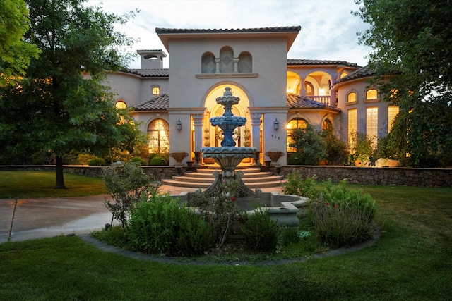 view of front of home featuring stucco siding, a tile roof, and a front lawn