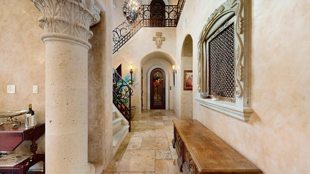 hall featuring stairway, decorative columns, stone tile floors, a towering ceiling, and arched walkways