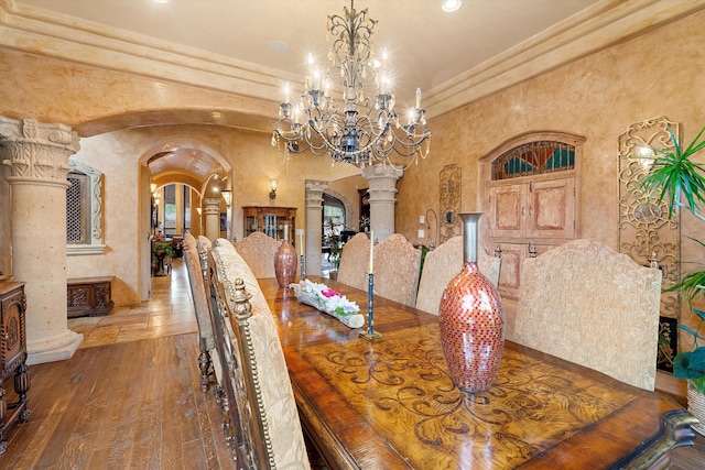 dining room with arched walkways, a chandelier, hardwood / wood-style floors, and decorative columns