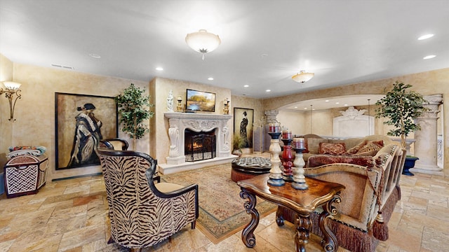 living area with visible vents, recessed lighting, a warm lit fireplace, arched walkways, and stone tile flooring