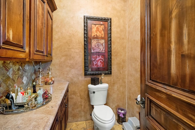 half bathroom with vanity, toilet, tasteful backsplash, and stone finish flooring