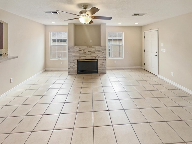 unfurnished living room featuring ceiling fan, light tile patterned floors, a textured ceiling, and a tile fireplace