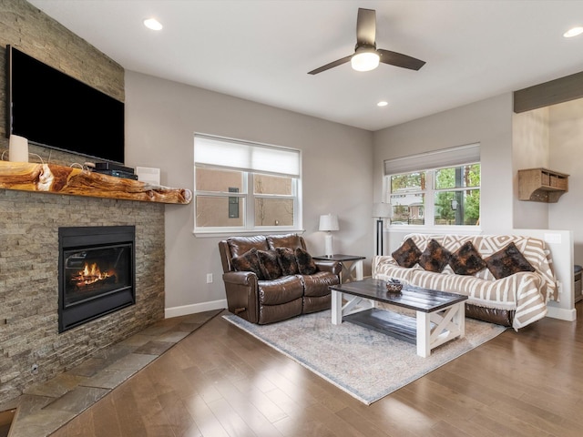 living room with dark hardwood / wood-style floors, a stone fireplace, and ceiling fan