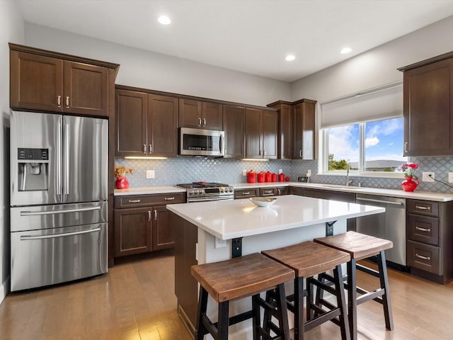 kitchen with a center island, stainless steel appliances, light hardwood / wood-style floors, a kitchen bar, and decorative backsplash