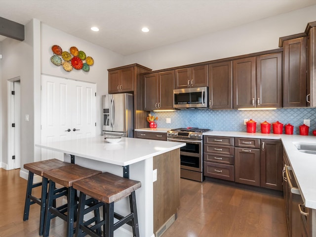 kitchen with backsplash, a kitchen breakfast bar, appliances with stainless steel finishes, a kitchen island, and dark hardwood / wood-style flooring