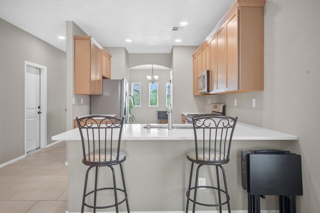 kitchen with a kitchen bar, light hardwood / wood-style floors, light brown cabinets, stainless steel appliances, and kitchen peninsula