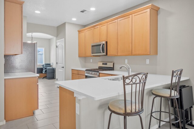 kitchen with kitchen peninsula, light brown cabinetry, and appliances with stainless steel finishes