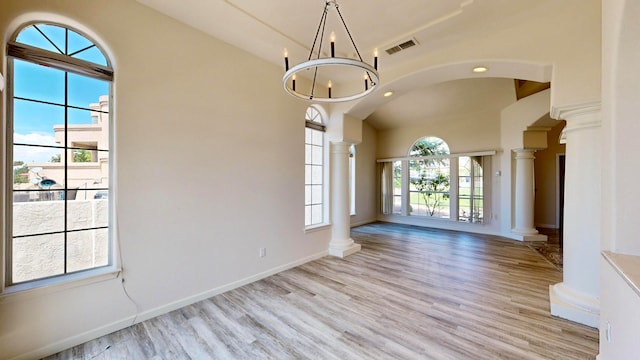 empty room with an inviting chandelier, ornate columns, plenty of natural light, and light hardwood / wood-style floors