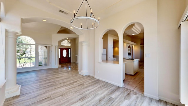 foyer entrance with a notable chandelier, decorative columns, and light hardwood / wood-style floors