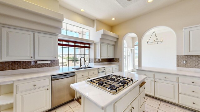 kitchen with appliances with stainless steel finishes, sink, pendant lighting, tasteful backsplash, and a kitchen island