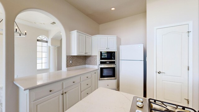 kitchen with oven, white cabinets, light stone countertops, white fridge, and black microwave