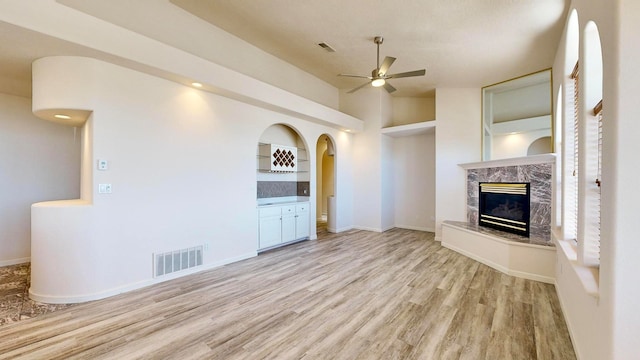 unfurnished living room featuring a high end fireplace, lofted ceiling, light hardwood / wood-style floors, built in shelves, and ceiling fan