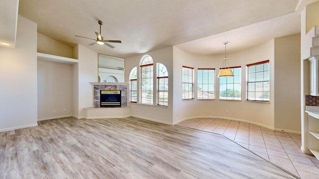 unfurnished living room with a textured ceiling, a high end fireplace, light wood-type flooring, vaulted ceiling, and ceiling fan