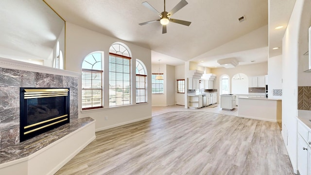 unfurnished living room with a premium fireplace, vaulted ceiling, ceiling fan, and light hardwood / wood-style floors