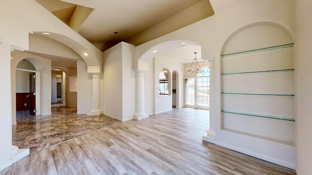 empty room featuring decorative columns, built in features, and light hardwood / wood-style floors