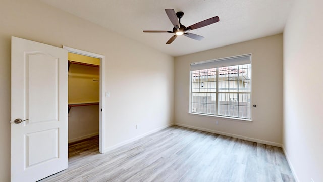 unfurnished bedroom with a walk in closet, light wood-type flooring, a closet, and ceiling fan