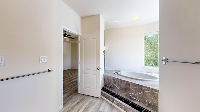 bathroom with ceiling fan, hardwood / wood-style flooring, and tiled tub