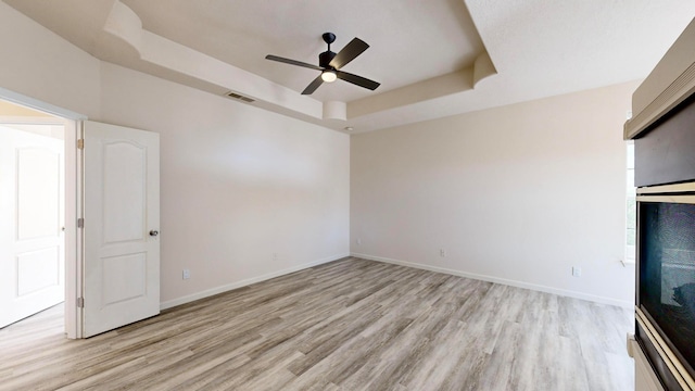 spare room featuring ceiling fan, light wood-type flooring, and a tray ceiling