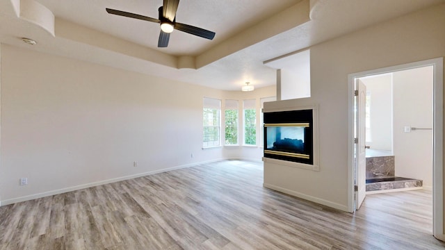 unfurnished living room with ceiling fan, a raised ceiling, and light hardwood / wood-style floors