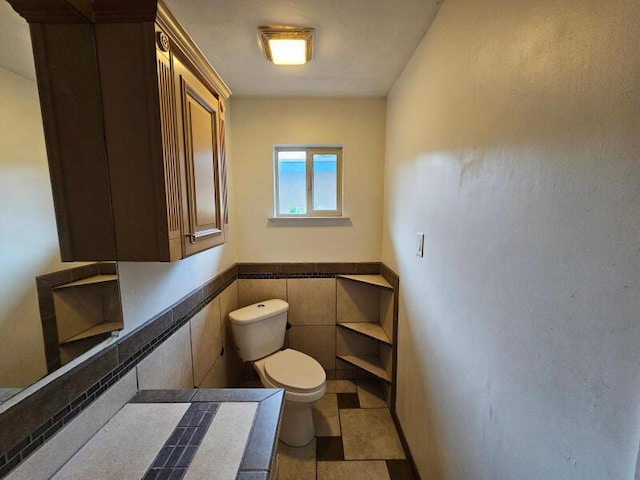 half bathroom with toilet, tile walls, wainscoting, and tile patterned flooring