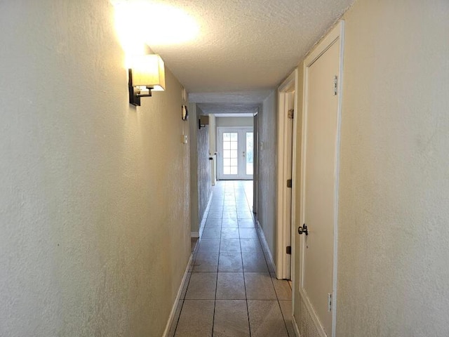 corridor with light tile patterned flooring, a textured wall, baseboards, and a textured ceiling