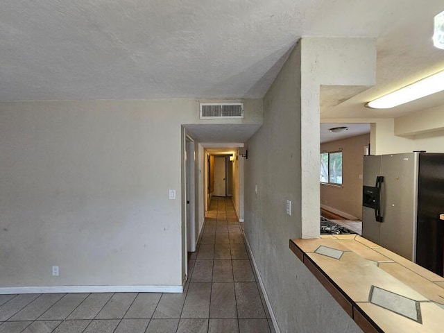 kitchen featuring visible vents, baseboards, stainless steel refrigerator with ice dispenser, tile patterned floors, and a textured ceiling