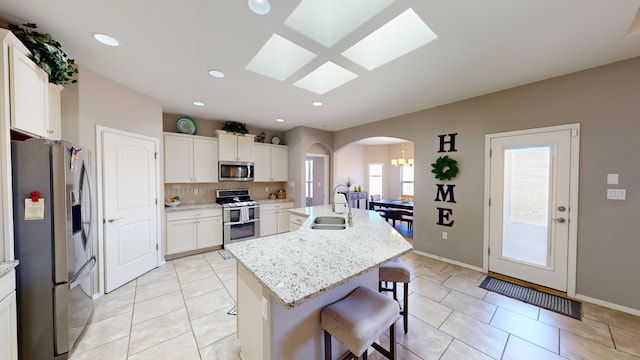 kitchen with stainless steel appliances, a center island with sink, white cabinets, and light tile patterned floors