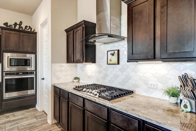 kitchen with light hardwood / wood-style flooring, decorative backsplash, light stone countertops, appliances with stainless steel finishes, and wall chimney range hood