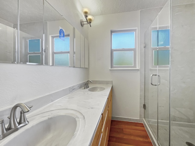 bathroom with a textured ceiling, wood finished floors, a sink, and a marble finish shower